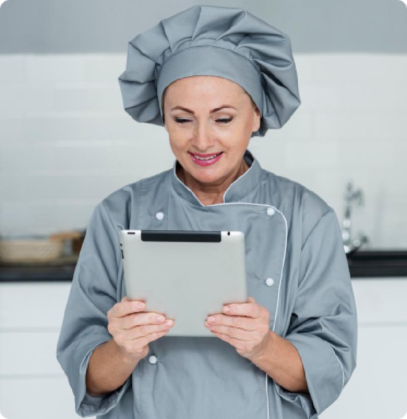une restauratrice souriante dans sa cuisine consultant les réservations sur sa tablette